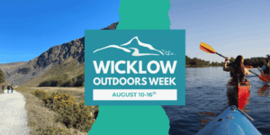 Wicklow Outdoors Week promotional banner featuring a central logo with the text "Wicklow Outdoors Week, August 10-16th". The background is split into two outdoor scenes: people walking on a trail in a rugged mountain valley on the left, and people kayaking on a calm river on the right.